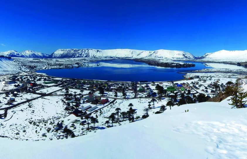 Fotografía panorámica de Caviahue con gente disfrutando de un evento al aire libre, con montañas nevadas y el lago de fondo. con gente disfrutando de un evento al aire libre, con montañas nevadas y el lago de fondo.