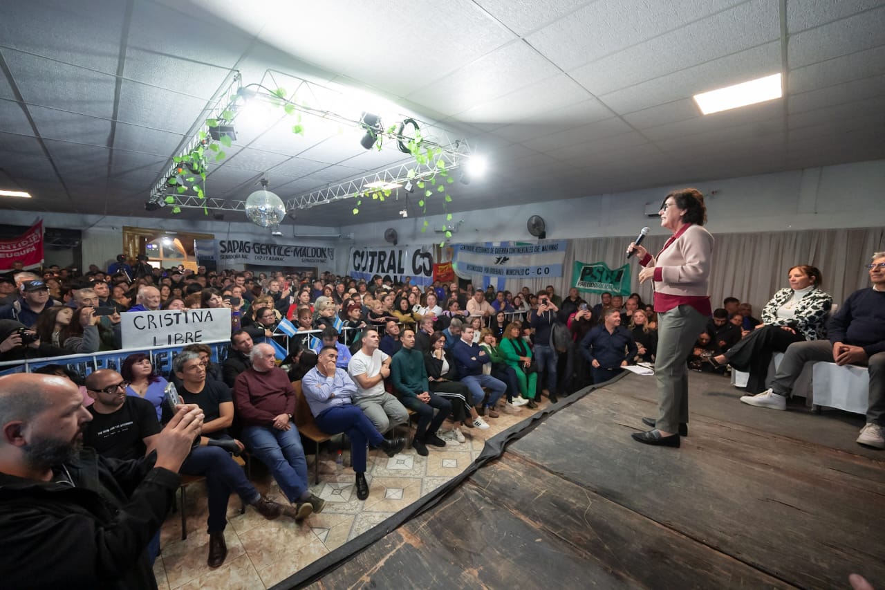 Foto de un acto político con personas escuchando a una oradora en un escenario.