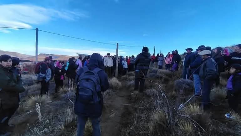  Alambrado perimetral rodeando un predio con carpas y asentamientos precarios, con una familia observando desde el interior.
