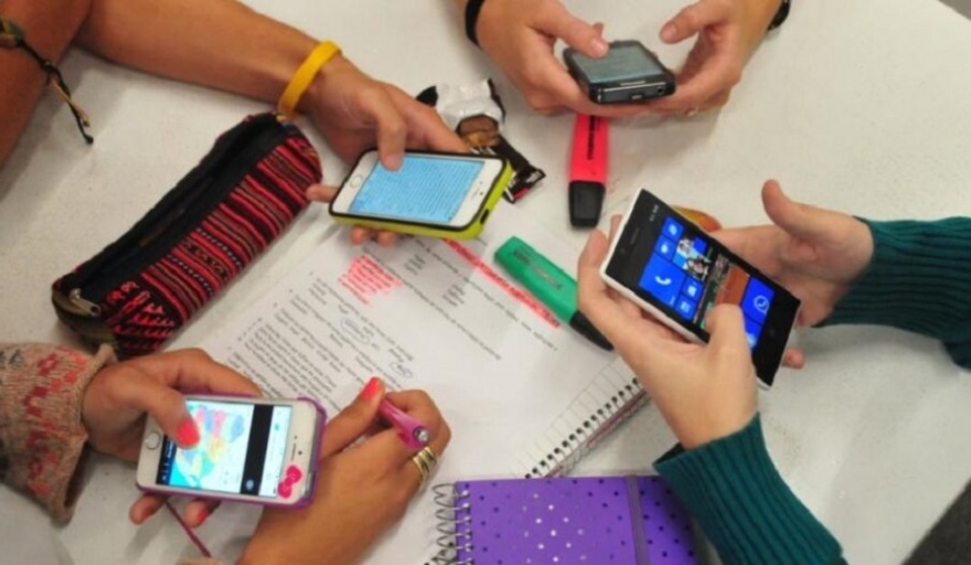 Estudiantes usando o guardando celulares en un entorno escolar, con un logo de prohibido o regulado.